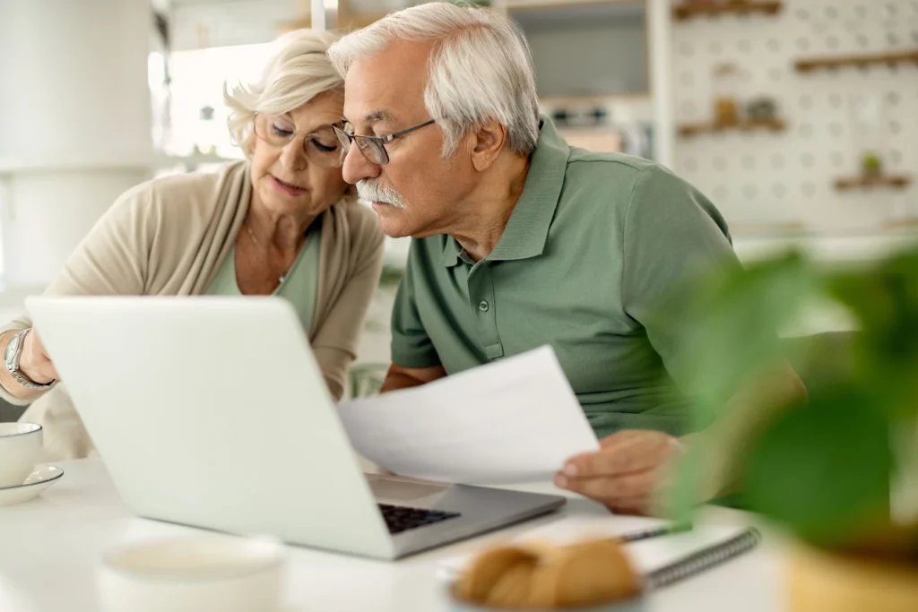 Casal de aposentados sentados em frente ao computador planejando renda passiva para ter uma aposentadoria sustentável