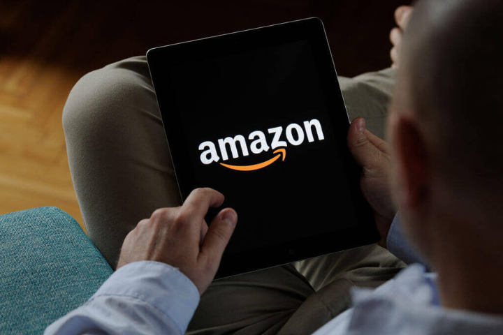 Foto de um homem sentado com a perna cruzada e segurando um tablet com a marca da Amazon