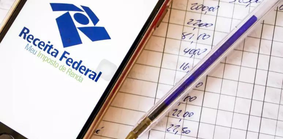 Celular com a logo da receita federal sobre cálculos no papel representando o informe sobre rendimentos