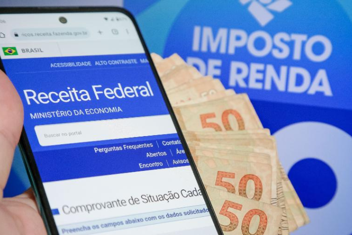foto de um celular aberto no site da receita federal, com notas de 50 reais atrás